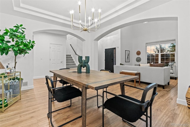 dining room with a chandelier, a raised ceiling, and light hardwood / wood-style flooring