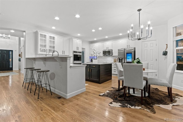 kitchen featuring stainless steel appliances, decorative light fixtures, light hardwood / wood-style floors, white cabinetry, and a breakfast bar area