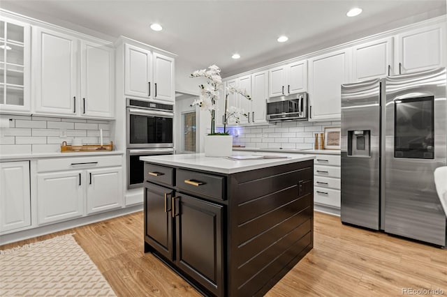 kitchen featuring appliances with stainless steel finishes, backsplash, light hardwood / wood-style flooring, white cabinets, and a kitchen island