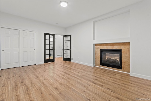 unfurnished living room with a tile fireplace, french doors, and light wood-type flooring