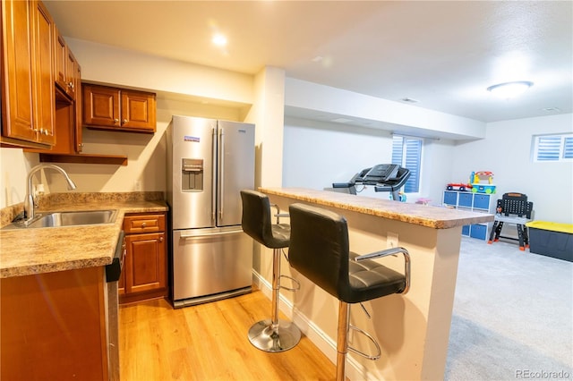 kitchen with high quality fridge, sink, a kitchen bar, kitchen peninsula, and light hardwood / wood-style flooring