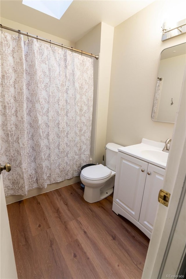 bathroom featuring wood-type flooring, toilet, vanity, and a skylight