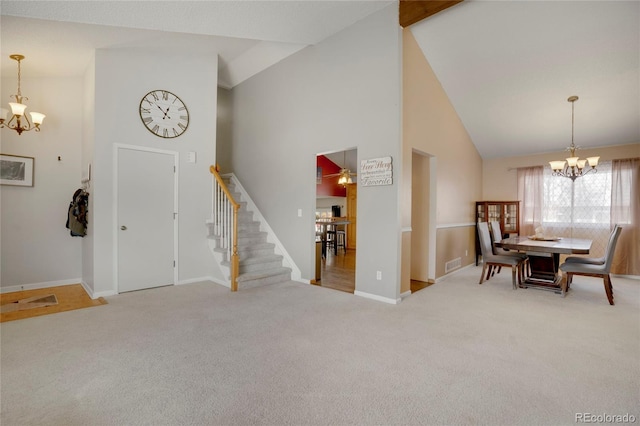 carpeted entryway featuring high vaulted ceiling, ceiling fan with notable chandelier, visible vents, baseboards, and stairway