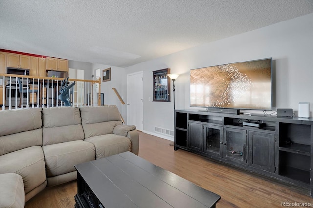 living room featuring visible vents, stairway, a textured ceiling, and wood finished floors