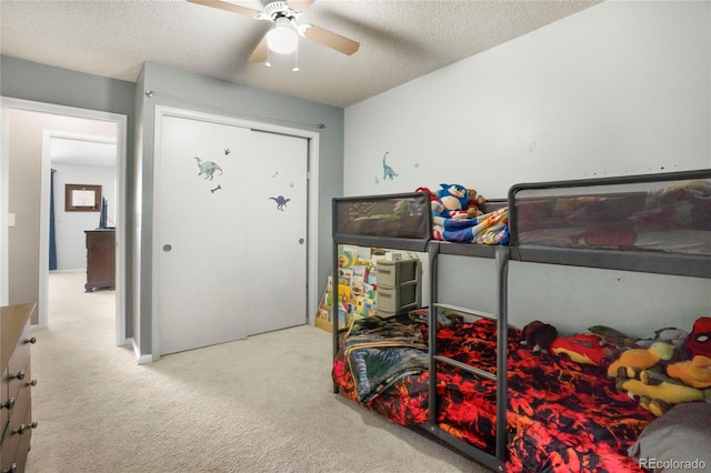 bedroom with a textured ceiling, ceiling fan, a closet, and carpet