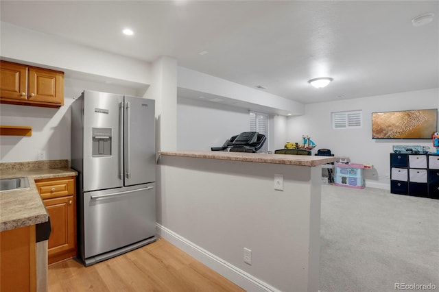 kitchen featuring stainless steel fridge with ice dispenser, light countertops, brown cabinetry, open floor plan, and baseboards