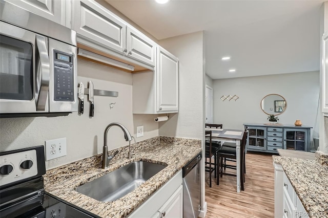 kitchen with white cabinetry, sink, stainless steel appliances, light stone counters, and light hardwood / wood-style flooring