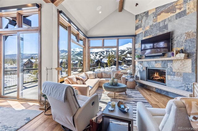 living room with high vaulted ceiling, a stone fireplace, beam ceiling, and wood finished floors