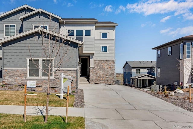 view of front of house with concrete driveway, stone siding, and board and batten siding