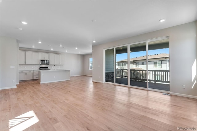 unfurnished living room featuring recessed lighting, light wood-style flooring, baseboards, and a sink
