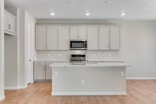 kitchen with range, stainless steel microwave, baseboards, and backsplash