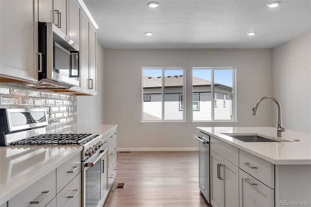 kitchen featuring light countertops, a sink, backsplash, light wood-style floors, and stainless steel appliances