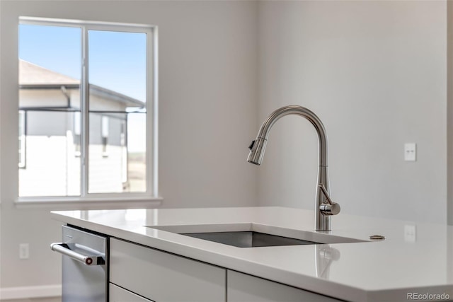 room details with stainless steel dishwasher, baseboards, a sink, white cabinetry, and light countertops