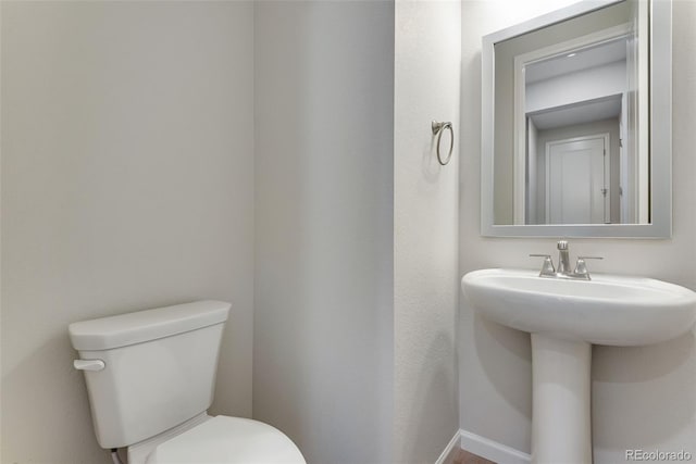 half bath featuring toilet, baseboards, and a sink