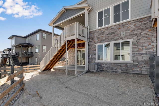 rear view of property featuring a deck, fence, stone siding, stairway, and central AC unit