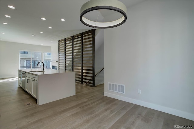 kitchen featuring light hardwood / wood-style floors, sink, white cabinets, and a center island with sink