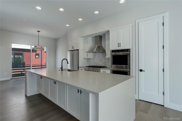 kitchen with appliances with stainless steel finishes, hardwood / wood-style floors, a center island with sink, and wall chimney range hood