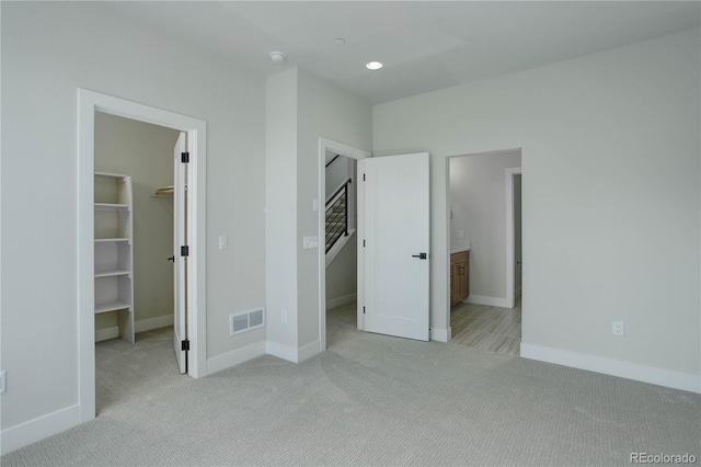 unfurnished bedroom featuring light colored carpet, a closet, ensuite bath, and a walk in closet