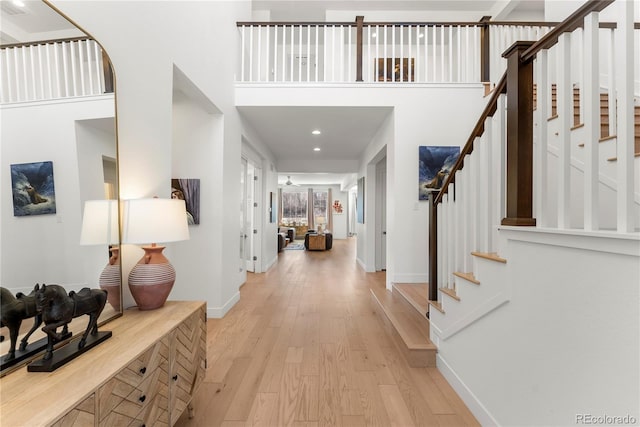 entrance foyer featuring light wood-type flooring, stairs, baseboards, and a towering ceiling