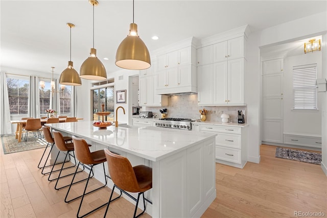 kitchen featuring light wood finished floors, range, a spacious island, a sink, and backsplash