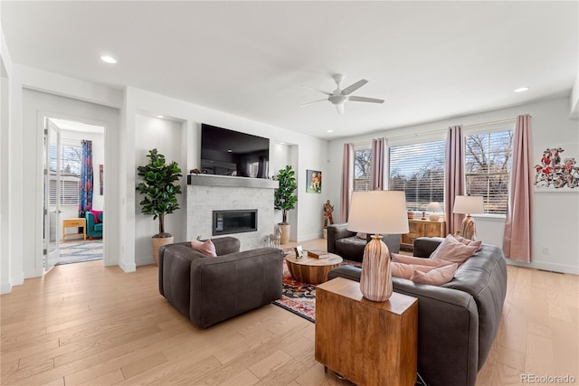 living room with a ceiling fan, a wealth of natural light, a fireplace, and light wood finished floors