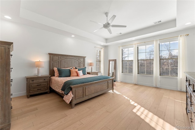 bedroom featuring light wood finished floors, visible vents, a tray ceiling, and baseboards