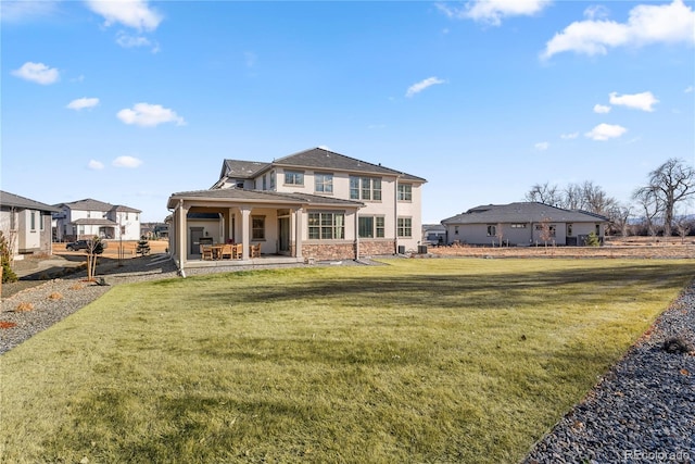 rear view of property featuring stone siding, a patio area, a lawn, and stucco siding