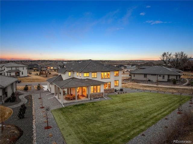 rear view of house featuring a patio, a tile roof, a yard, stone siding, and a residential view