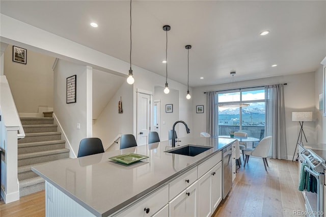 kitchen with appliances with stainless steel finishes, light hardwood / wood-style floors, an island with sink, white cabinets, and sink