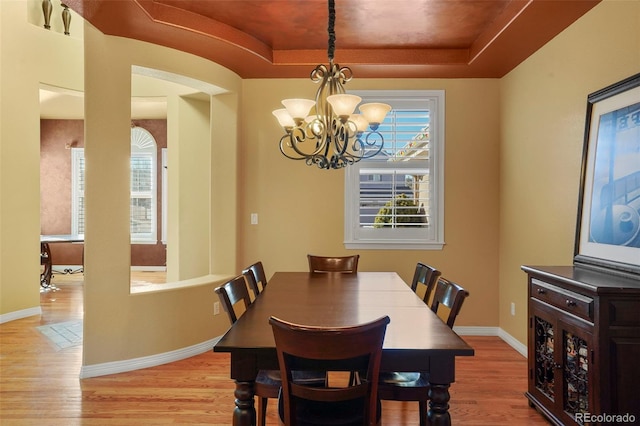 dining space featuring an inviting chandelier, light hardwood / wood-style flooring, and a raised ceiling