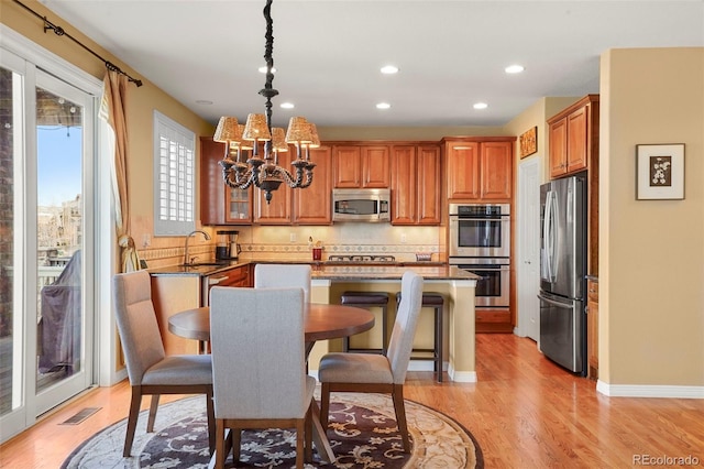 kitchen with a breakfast bar area, a center island, hanging light fixtures, stainless steel appliances, and light hardwood / wood-style floors