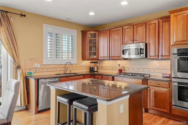 kitchen featuring sink, light hardwood / wood-style flooring, appliances with stainless steel finishes, a kitchen island, and dark stone counters