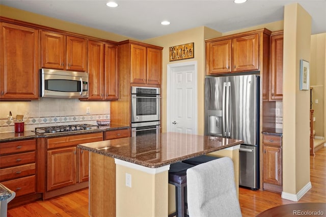 kitchen with appliances with stainless steel finishes, tasteful backsplash, dark stone counters, a center island, and light hardwood / wood-style floors