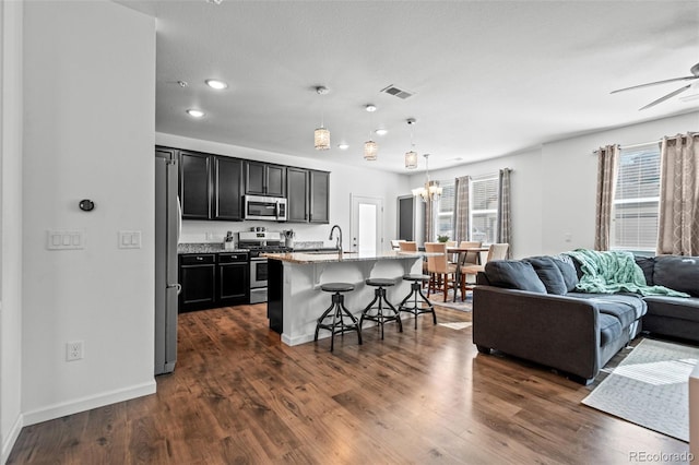 kitchen featuring visible vents, open floor plan, a kitchen island with sink, stainless steel appliances, and a kitchen bar