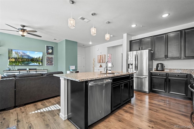 kitchen featuring stainless steel appliances, visible vents, open floor plan, hanging light fixtures, and a center island with sink