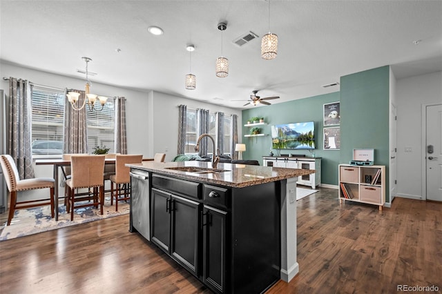 kitchen featuring a sink, dark cabinetry, light stone countertops, an island with sink, and decorative light fixtures