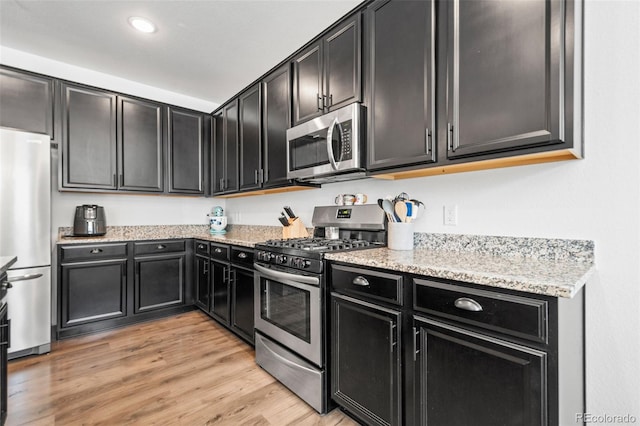 kitchen with light wood-style flooring, recessed lighting, dark cabinets, appliances with stainless steel finishes, and light stone countertops