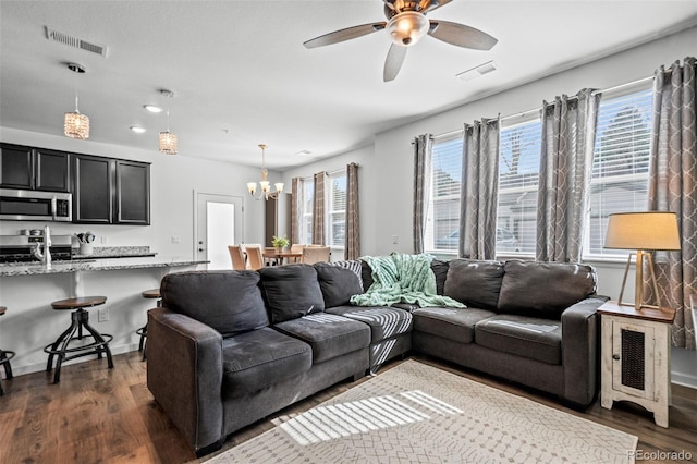 living room featuring plenty of natural light, visible vents, dark wood-style flooring, and ceiling fan with notable chandelier