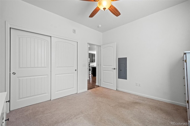 unfurnished bedroom featuring a closet, light colored carpet, a ceiling fan, electric panel, and baseboards