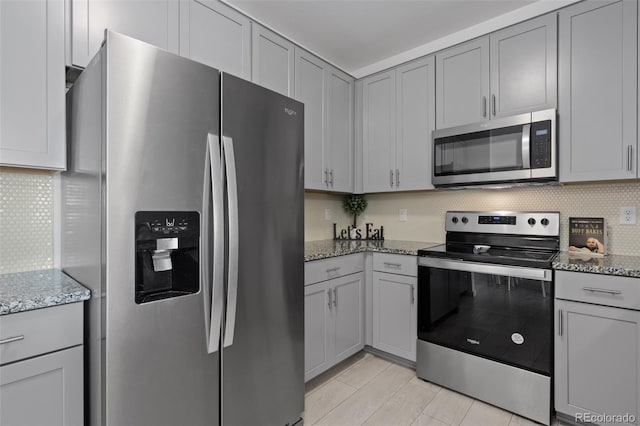 kitchen featuring stainless steel appliances, light stone countertops, gray cabinetry, and decorative backsplash