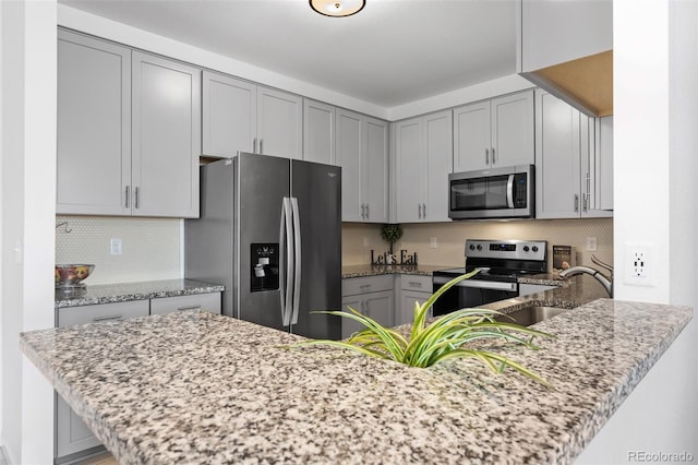 kitchen with light stone countertops, appliances with stainless steel finishes, and gray cabinetry