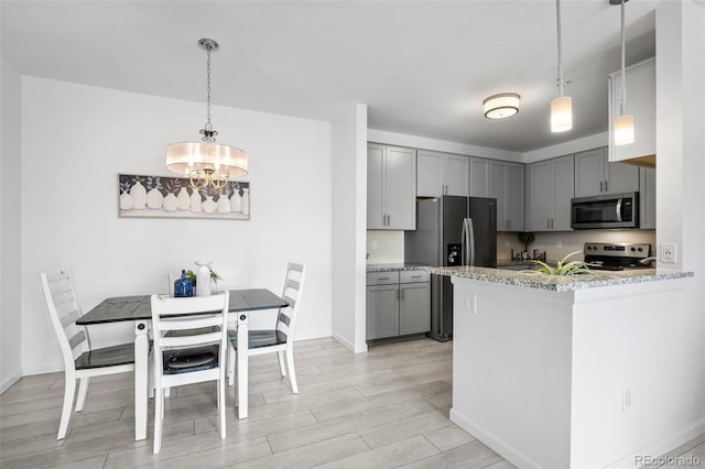 kitchen featuring wood finish floors, light stone countertops, gray cabinets, appliances with stainless steel finishes, and hanging light fixtures