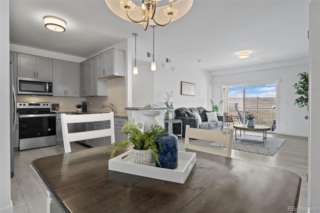 kitchen featuring gray cabinetry, open floor plan, light wood-style flooring, a notable chandelier, and stainless steel appliances