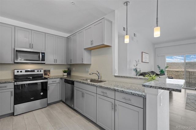 kitchen featuring a sink, a peninsula, light stone counters, gray cabinetry, and appliances with stainless steel finishes