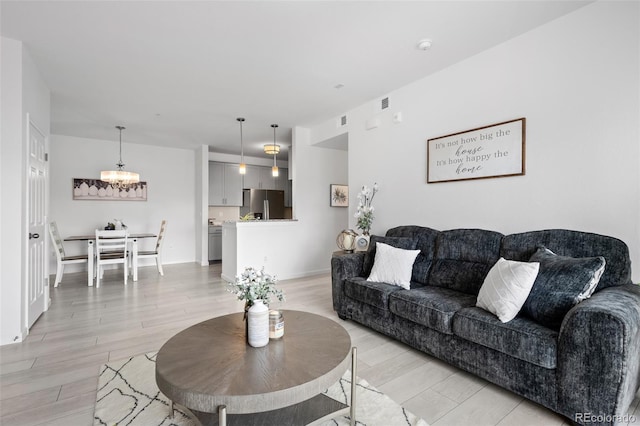 living room with an inviting chandelier, light wood-style flooring, baseboards, and visible vents