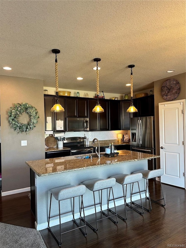 kitchen featuring decorative backsplash, a kitchen island with sink, a kitchen breakfast bar, a textured ceiling, and appliances with stainless steel finishes