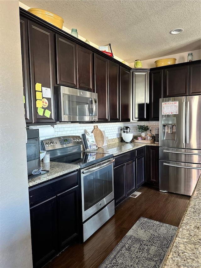 kitchen with stainless steel appliances, a textured ceiling, dark wood finished floors, and tasteful backsplash