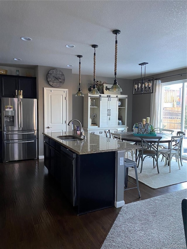 kitchen with dark wood-style flooring, black dishwasher, stainless steel refrigerator with ice dispenser, light stone counters, and a sink