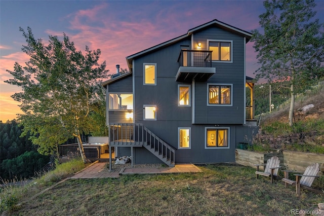 back house at dusk featuring a patio, a balcony, and a lawn