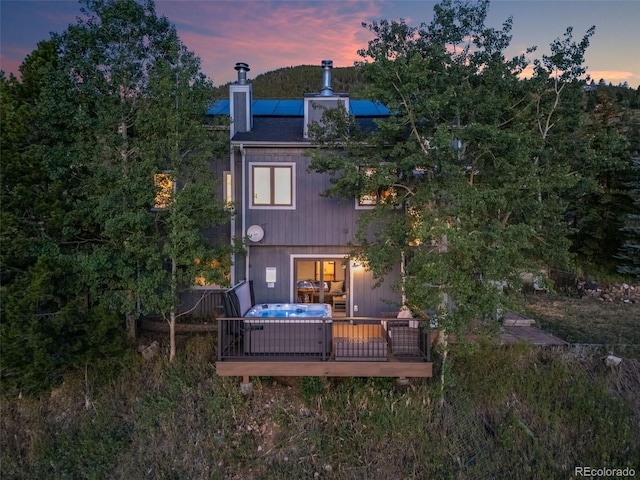 back house at dusk with a hot tub, solar panels, and a deck